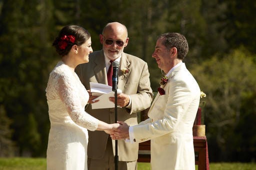 In this March 2014 photo provided by Eva Zimmerman, Zimmerman, left, and Noah Schreck, join hands as Eva's stepfather Jack Shoemaker officiates their wedding ceremony in Berkeley, Calif. (Erich Valo/Magnolia Weddings/Eva Zimmerman via AP)