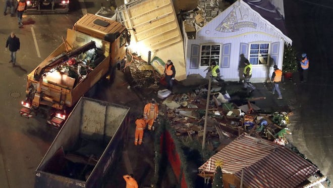 Road sweepers stay beside debris between the huts of a Christmas market beside the memorial church in Berlin on Wednesday, two days after a truck ran into a crowded Christmas market and killed several people. (AP Photo/Michael Sohn)