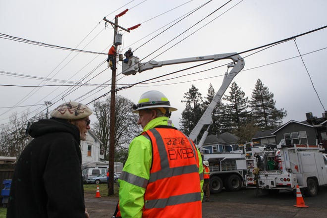 Michael Forster (left) talks with Mark Maguire as crews work to restore power to his neighborhood. (Kelly Lyon/The Register-Guard)