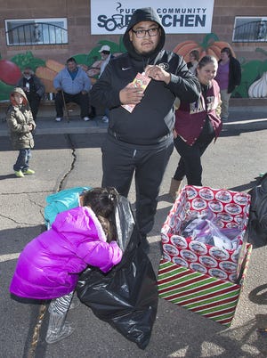 CHIEFTAIN PHOTO/JOHN JAQUES Three-year-old Jaylnn Martinez (in blue) and sister Jordan, 5, dive into a bag of Christmas presents at the Pueblo Community Soup Kitchen Saturday, while their dad Julio Martinez looks on.