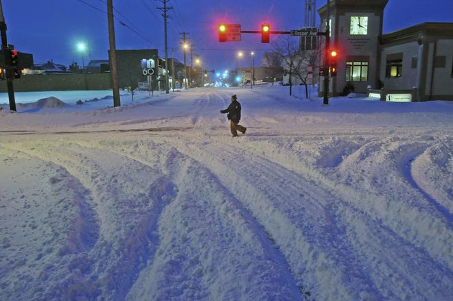 Madori Griffin, who says her car was snowed in, makes her way through an intersection while walking to work in the intensive care unit of Sanford Hospital early Monday, Dec. 26, 2016, in Bismarck, N.D. The combination of freezing rain, snow and high winds that forced the shutdown Sunday of vast stretches of highways in the Dakotas continued into Monday morning, and authorities issued no-travel warnings for much of North Dakota. (Tom Stromme/The Bismarck Tribune via AP)