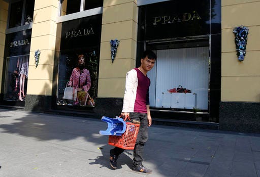 A shoeshine man walks past a Prada fashion store in downtown Hanoi, Vietnam, Wednesday, Dec. 28, 2016. Vietnam's economy is forecast to grow 6.2 percent in 2016, helped by a manufacturing and building boom. The General Statistics Office said Wednesday that this year's growth rate is below 2015's rate of 6.7 percent but is still considered a success given unfavorable global trends and a spate of natural and environmental disasters. (AP Photo/Tran Van Minh)