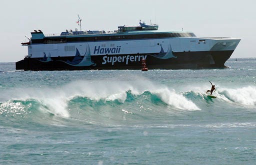 FILE - In this June 30, 2007, file photo, a surfer catches a wave at Kakaako Waterfront Park as the Hawaii Superferry approaches Aloha Towers in Honolulu. Hawaii officials are exploring what it would take to run a ferry between islands. But they're facing skepticism over costs and whether there's a ferry system residents would accept. But the idea is bringing back memories of the Superferry, an emotional and expensive failure in Hawaii history. Years ago protesters blocked the Superferry from docking in Kauai. And a court later ordered the ferry to stop running because the state didn't do a proper environmental review. (AP Photo/Marco Garcia, File)