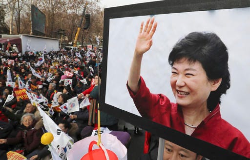 A supporter holds a picture of South Korean President Park Geun-hye as others hold their national flags during a rally opposing her impeachment in Seoul, South Korea, Saturday, Dec. 31, 2016. The Constitutional Court has up to six months to decide whether Park should permanently step down over a corruption scandal or be reinstated. (AP Photo/Lee Jin-man)
