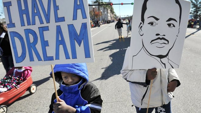 Tyron White and Blessed Rhymer hold signs as they make their way down the route of the Martin Luther King Jr. Day parade in Jacksonville, Fla., in 2016.