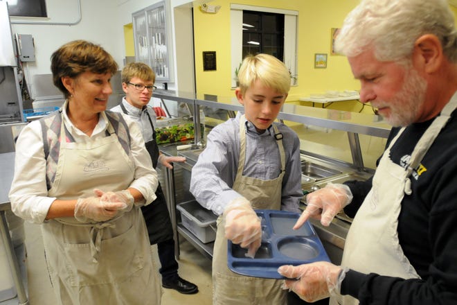 Sandy Codington, left, looks on as her husband John help brothers Ilya (back) and Peter Gilman prepare to serve a Thanksgiving Day meal to the less fortunate at the Good Shepherd Center alongside other First Presbyterian Church members in 2015. STARNEWS FILE
