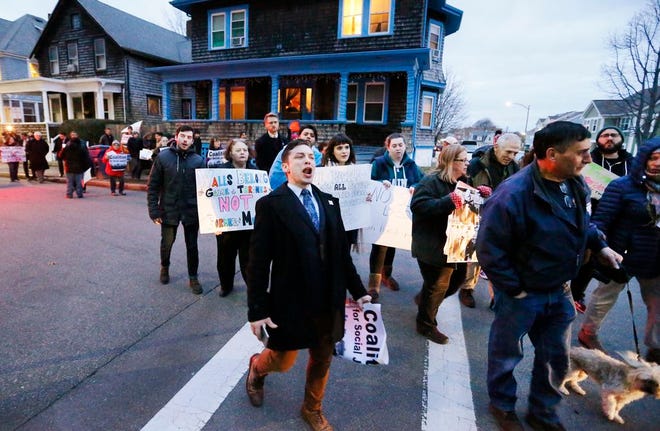 Demonstrators, protesting Sheriff Tom Hodgson's plan to send inmates to Texas to help build President-elect Donald Trump's wall along the Mexico-United States border, walk along Ash Street, adjacent to the Ash Street Jail in New Bedford on Thursday.