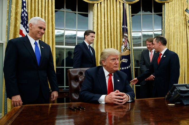 Vice President Mike Pence, left, watches as President Donald Trump prepares to sign his first executive order on Jan. 20 in the Oval Office.