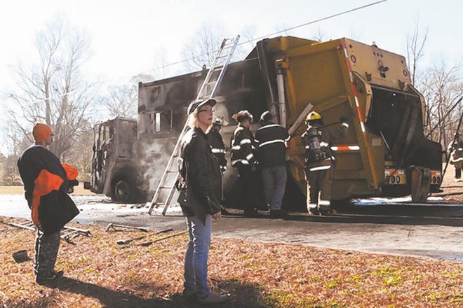 First Responders from Stella, Hubert, Swansboro and West Carteret fire companies attempt to pry open an M&W Hauling garbage truck that caught fire Wednesday morning. The driver of the truck, Mitch Barbour, pictured left, escaped without injury. Patty Lambert, the owner of M&W Hauling, a Hubert-based waste removal company, is standing to Barbour's right awaiting a replacement truck to complete the morning route. Photo by Mike McHugh / The Daily News