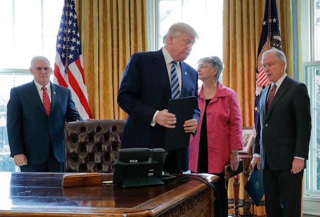 President Donald Trump holds a freshly signed an executive order in the Oval Office of the White House in Washington, Thursday, Feb. 9, 2017, as Vice President Mike Pence, left, Attorney General Jeff Sessions, left, and Sessions' wife Mary watch. Trump signed three executive orders related to reducing crime after participating in Sessions' swearing in ceremony.