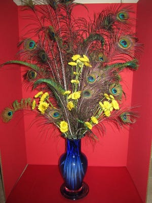 GGC Member Lorraine Gautreau presented a graceful floral design of peacock tail feathers and yellow mums in a tall clear blue glass vase.