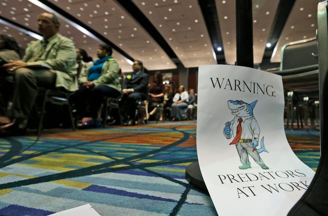 A sign warning of predatory payday lenders leans up against a chair during a speech by Consumer Financial Protection Bureau Director Richard Cordray, in Richmond, Va., March 26, 2015. (AP Photo/Steve Helber)