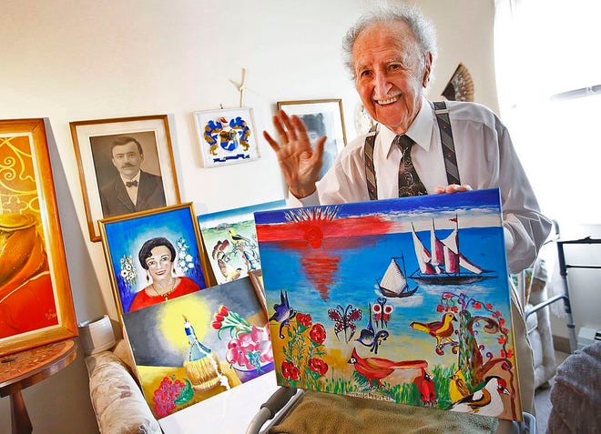 Armando Peduzzi, 92, of Quincy with some of the colorful and fanciful paintings he has done for children. The black-and-white photograph on the wall is of his father in Italy.