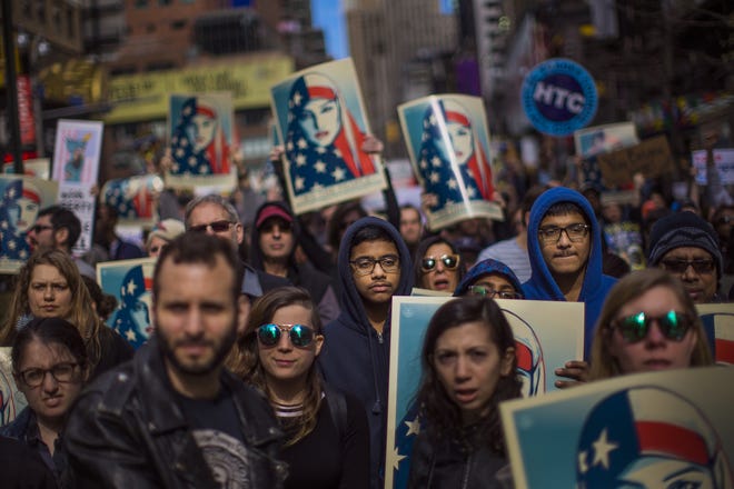 People carry posters during a rally in support of Muslim Americans and protest of President Donald Trump's immigration policies in Times Square, New York on Sunday. [ANDRES KUDACKI / ASSOCIATED PRESS]