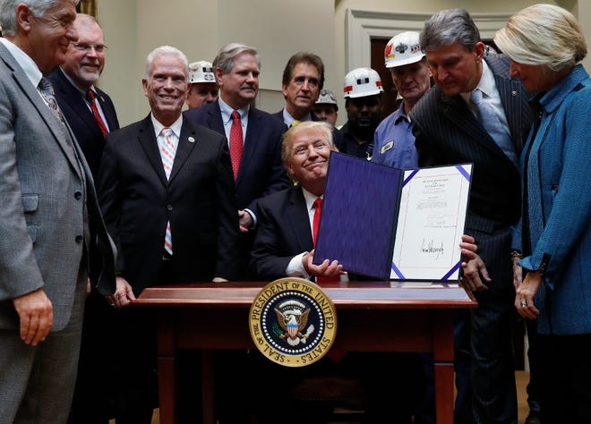 President Donald Trump, joined by coal miners and members of Congress including Sen. Shelley Moore Capito, R-W. Va., right, Sen. Joe Manchin, D-W. Va., second from right, and Rep. Bill Johnson, R-Ohio, third from right, holds up H.J. Res. 38 after signing it in the Roosevelt Room of the White House in Washington, Thursday, Feb. 16, 2017.