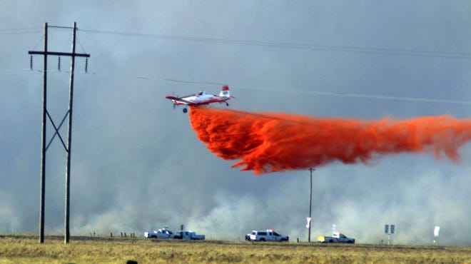 A crop duster drops fire retardant on a wildfire near the Fritch Highway at dusk on Monday. (Photo by Neil Starkey)