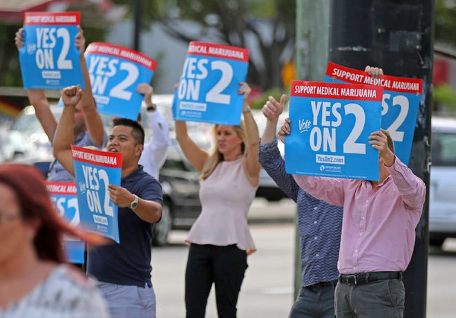 Supporters of an amendment to legalize medical marijuana for ailments including glaucoma, AIDS and post-traumatic stress disorder wave signs at passing traffic at a street corner in Fort Lauderdale on Nov. 8, 2016.
