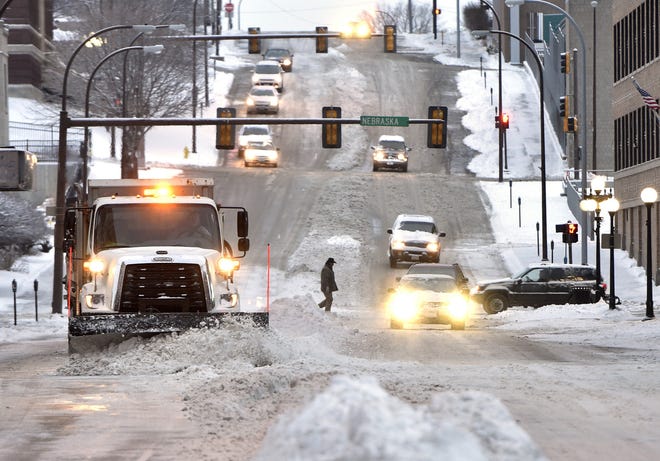 A pedestrian crosses the street as a city snowplow works to widen a lane in Sioux City, Iowa, Monday, March 13, 2017. Nearly 9 inches of snow has been reported in northeast Iowa's Black Hawk County from a late-winter storm that's hampering travelers. THE ASSOCIATED PRESS