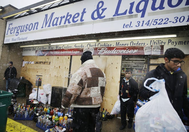 In this Wednesday, Nov. 26, 2014, file photo, Kush Patel, right, carries out bags of merchandise while helping his uncle Andy Patel, rear, clean up the looting damage from riots at his store, Ferguson Market and Liquor, in Ferguson, Mo. The store is disputing a new documentary's claims that surveillance video suggests Michael Brown didn't rob the store before he was fatally shot by police in Ferguson. THE ASSOCIATED PRESS