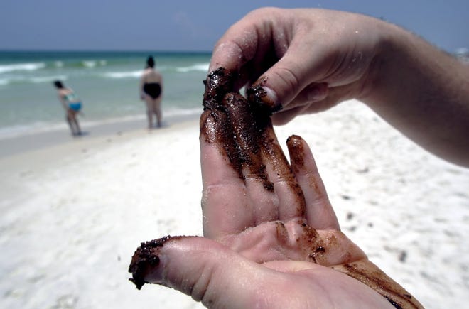 A visitor from Minnesota spreads tar balls from the Deepwater Horizon oil spill on his hands in Panama City Beach in June 2010. [NEWS HERALD FILE PHOTO]