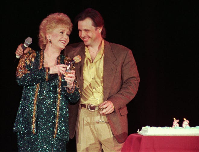 FILE - In this April 1, 1997, file photo, Debbie Reynolds, left, celebrates her 65th birthday on stage as her son, Todd Fisher, presents her with a cake following her evening variety show, at the Debbie Reynolds Hotel in Las Vegas. Fisher told Entertainment Tonight for an interview published online on March 22, 2017, that Reynolds set him up “for her leaving the planet” the day his sister and Reynolds’ daughter Carrie Fisher died in December 2016. (AP Photo/Lennox McLendon, File)
