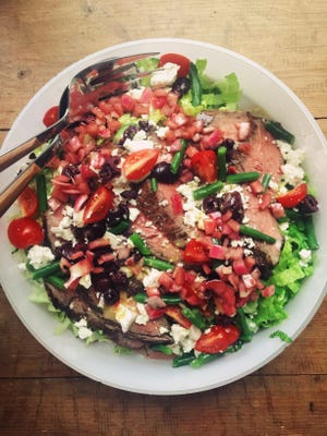 A few slices of pink, perfectly cooked steak draped across a colorful bowl of Greek salad make a lunch or dinner that knows no season. [Katie Workman via AP]