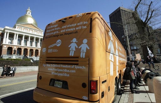 Protesters, right, hold signs beside the "Free Speech Bus"outside the Statehouse Thursday in Boston. [AP Photo]