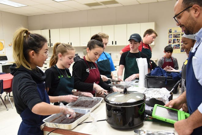 Weed Elementary School students work with teacher's aide Eriksson Bioso March 30, 2017 preparing food made from scratch by the cooking class for volunteers who are in town working on Habitat for Humanity houses. By Liz Pyles