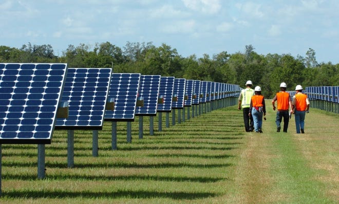 Workers walk down a row of photovoltaic panels at Florida Power & Light's solar power plant in DeSoto County. [Mike Lang/Herald-Tribune]