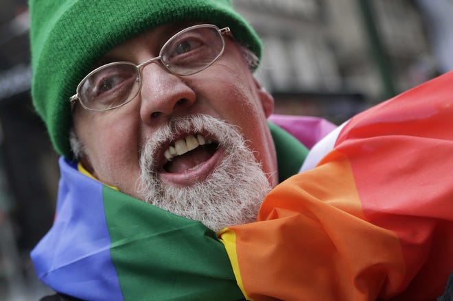 Artist Gilbert Baker, designer of the rainbow flag, is draped with the flag while protesting at the St. Patrick's Day parade in New York in 2014. Baker, creator of the flag that has become a widely recognized symbol of gay rights, has died at age 65. [AP FILE PHOTO]
