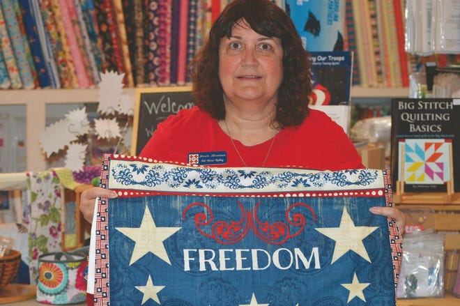 Kirsta Meadows, owner of All about Quilts and whose son was injured in Fallujah, shows off one of the many Quilts of Valor that are donated to local veterans. Photo by Alan Lane / The Daily News