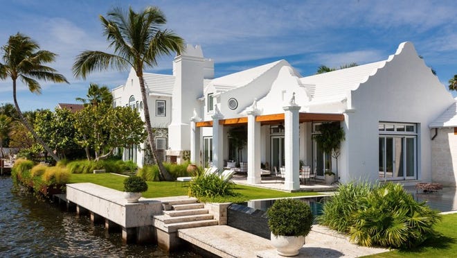 At the rear of the residence, the main portion of the house features a medley of Bermudan architectural details, from scalloped gables to an outdoor fireplace to dormer windows on the second floor. Doors in the covered loggia lead into the living room. The coral keystone steps lead down to a gondola-style dock. Photo by Sargent Architectural Photography