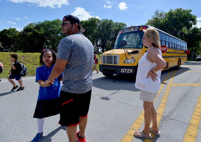 Parents stand in the middle of the road as children cross the street at a bus stop on Grand Island Shores Road on Tuesday in Eustis. Parents stand in the street to make sure that children are able to cross safely. [AMBER RICCINTO / DAILY COMMERCIAL]