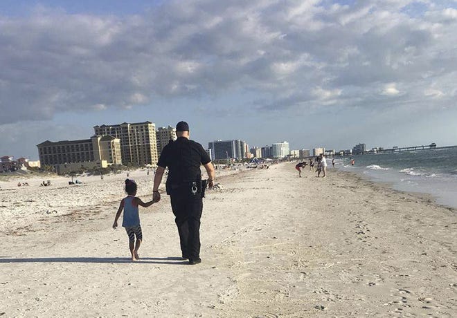 In this April 11, 2017, image provided by Amy Amerell, Clearwater police officer Rich Edmonds holds the hand of a 6-year-old girl on Clearwater Beach, Fla. The girl wandered away from her family and approached another family who called police for assistance. When the child refused to get in the officer's car, he walked her down the beach until they found her family. (Courtesy of Amy Amerell via AP)