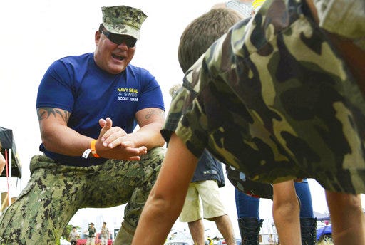 This 2016 photo provided by the U.S. Navy shows Chief Petty Officer Joseph Schmidt III, assigned to the Navy SEAL and SWCC Scout Team, encouraging a young fan to do pushups at the 2016 Stuart Air Show in Stuart, Fla. The Navy is investigating Schmidt, a decorated SEAL who moonlights as a porn actor. The Naval Special Warfare Command is investigating whether Schmidt properly sought permission from his commanders for outside work, whether they condoned it and whether Schmidt engaged in behavior that discredits the service.