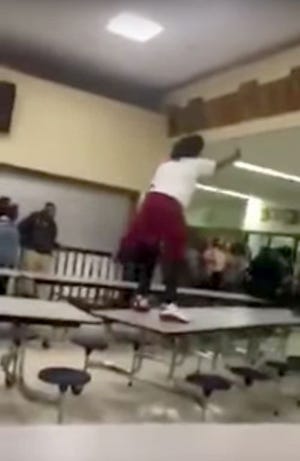 A screen grab from a YouTube video shows a Peoria High School student, allegedly armed with a knife, standing atop a cafeteria table moments before a Peoria police officer subdued her with a stun gun.