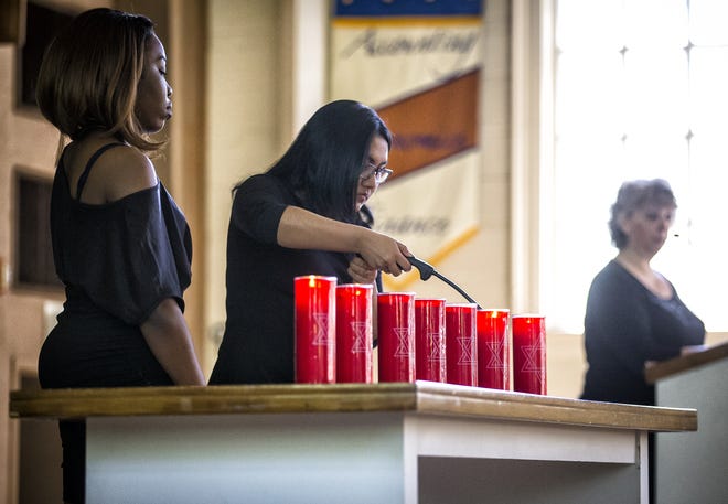 Illinois College students Dristi Shrestha, center, and Maria Owumi, left, light one of the seven candles remembering the lives lost in the Holocaust during a commemoration program on Monday at the college. [Justin L. Fowler/The State Journal-Register]