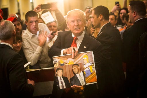 In this 2016 file photo, Republican presidential candidate Donald Trump holds depictions of himself on, "The Simpsons" and a photo with boxer Mike Tyson, given to him by an attendee during a campaign stop at the Radisson Hotel in Nashua, N.H. "The Simpsons" released a short online clip on April 26, mocking President Donald Trump ahead of his 100th day in office.