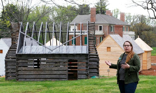 In this Wednesday, April 12, 2017 photo, Jennifer Glass, director of Archeology and Historical Preservation at James Madison's estate, gestures in front of some of the reconstructed slave cabins in the South Yard of the property in Montpelier, Va. Crews at Montpelier, the mansion in the foothills of the Blue Ridge Mountains, are excavating and reconstructing six structures on what’s called the South Yard, where domestic slaves lived and worked. (AP Photo/Steve Helber)
