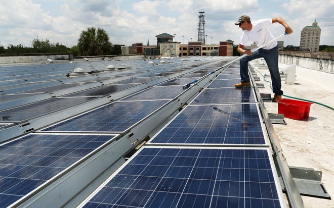 A technician cleans solar panels atop a building in downtown Gainesville. [File]