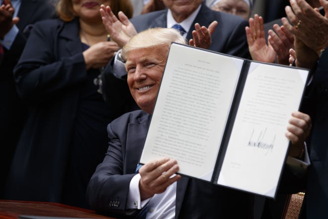 President Donald Trump holds up a signed executive order aimed at easing an IRS rule limiting political activity for churches, Thursday, May 4, 2017, in the Rose Garden of the White House in Washington. THE ASSOCIATED PRESS