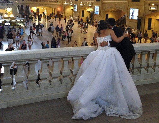 FILE - In this Aug. 8, 2014, file photo, a bride and groom lean over the east balcony as they pose for a photograph in Grand Central Terminal in New York. If you’re busy planning a wedding, you might want to consider insuring it. Wedding insurance policies are relatively easy to understand, and the two main types, liability and cancellation, are both inexpensive compared with the cost of a ceremony and reception. (AP Photo/Donald King, File)