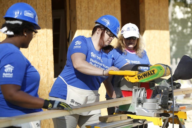Jane Anderson, center, a volunteer with Habitat of Humanity's Women Build program, cuts a board with a chop saw as other volunteers Karen Bailey, left, and Sharon Hiemenz, a board member of Habitat of Humanity, work on building a new home for Tonya Kelly-Scott in High Springs Saturday. The work was part of National Women Build Week 2017. [Brad McClenny/Staff photographer]