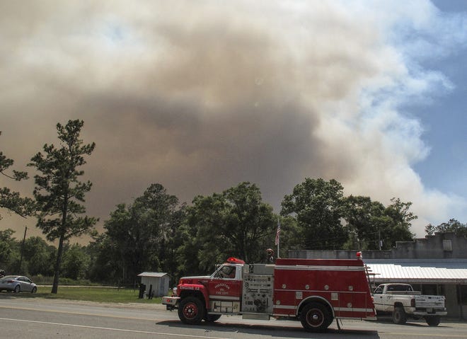 A fire truck passes as a plume of smoke rising from a wildfire burning, Monday, May 8, 2017, just outside the town of St. George, Ga. Officials placed the town under a mandatory evacuation after winds pushed the fire out of the neighboring Okefenokee National Wildlife Refuge, where a lightning strike started the blaze a month earlier. (AP Photo/Russ Bynum)