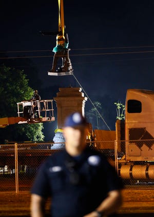 The figure of Jefferson Davis is removed from its base as a police officer stands watch over demonstrators both for and against the removal of confederate era statues in New Orleans, Thursday, May 11, 2017. (AP Photo/Gerald Herbert)