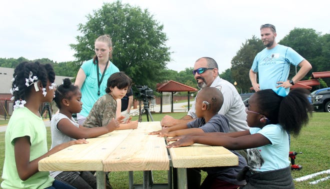 Students at the S.C. School for the Deaf and the Blind test out the table built by Croft State Park employee Jason Hege, seated, and Chad Adams, standing at right. [SAMANTHA SWANN/SPARTANBURG HERALD-JOURNAL]