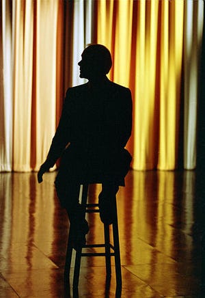 Talk show host Johnny Carson sits on a stool center stage as he watches clips from earlier shows during the last taping of the "Tonight Show" in front of family and friends in Burbank, Ca., Friday, May 22, 1992. The king of late-night television ends his 30-year reign on NBC. [AP Photo/Douglas C. Pizac]
