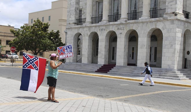 Carol Mize holds a Mississippi flag and a sign as she protests outside City Hall in Biloxi, Miss., on May 18 against Mayor Andrew "FoFo" Gilich's decision to remove the state flag from display at city buildings because it contains the Confederate battle emblem. (AP Photo /Emily Wagster Pettus)