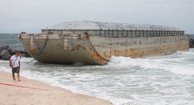 A beachgoer searches for metal in the sand after this empty hopper barge broke free from its transport and washed ashore during rough weather near the jetties Wednesday at St. Andrews State Park in Panama City Beach. [PATTI BLAKE/THE NEWS HERALD]