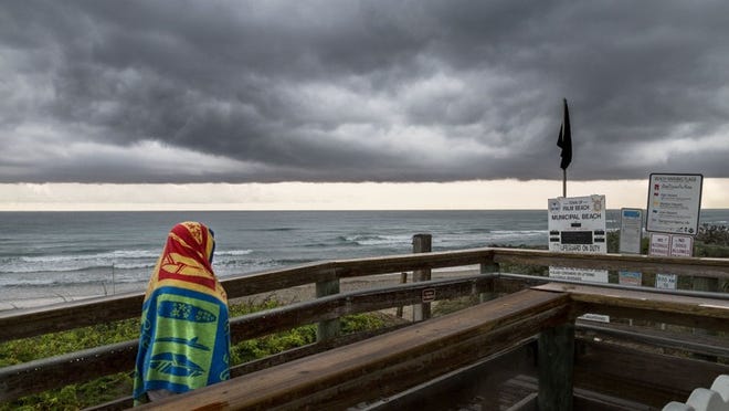 A beachgoer seeks shelter from the rain after a morning on Midland Beach in Palm Beach. (Greg Lovett / The Palm Beach Post)